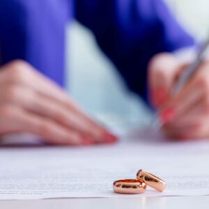 anillos de boda en primer plano, mujer firmando un documento en el fondo, contratos domésticos, derecho de familia de Florida