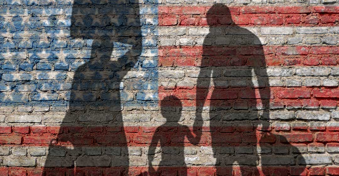 silueta de la familia que lleva el equipaje con la bandera de EE.UU. pintado en la pared de ladrillo, petición de la familia