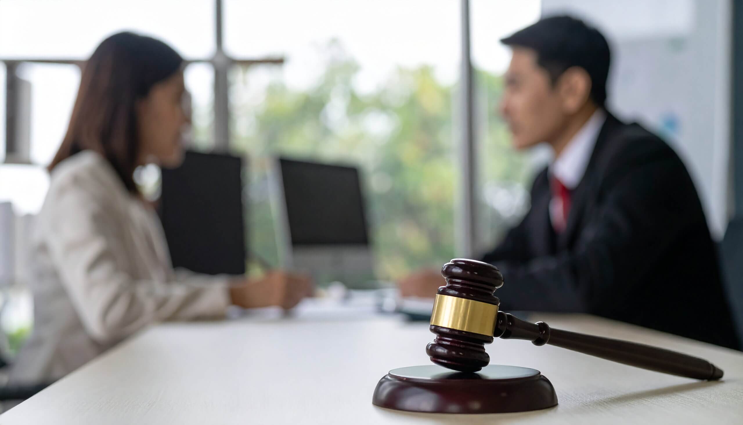 Abogada asesorando a cliente en oficina con mazo judicial sobre la mesa durante consulta legal.